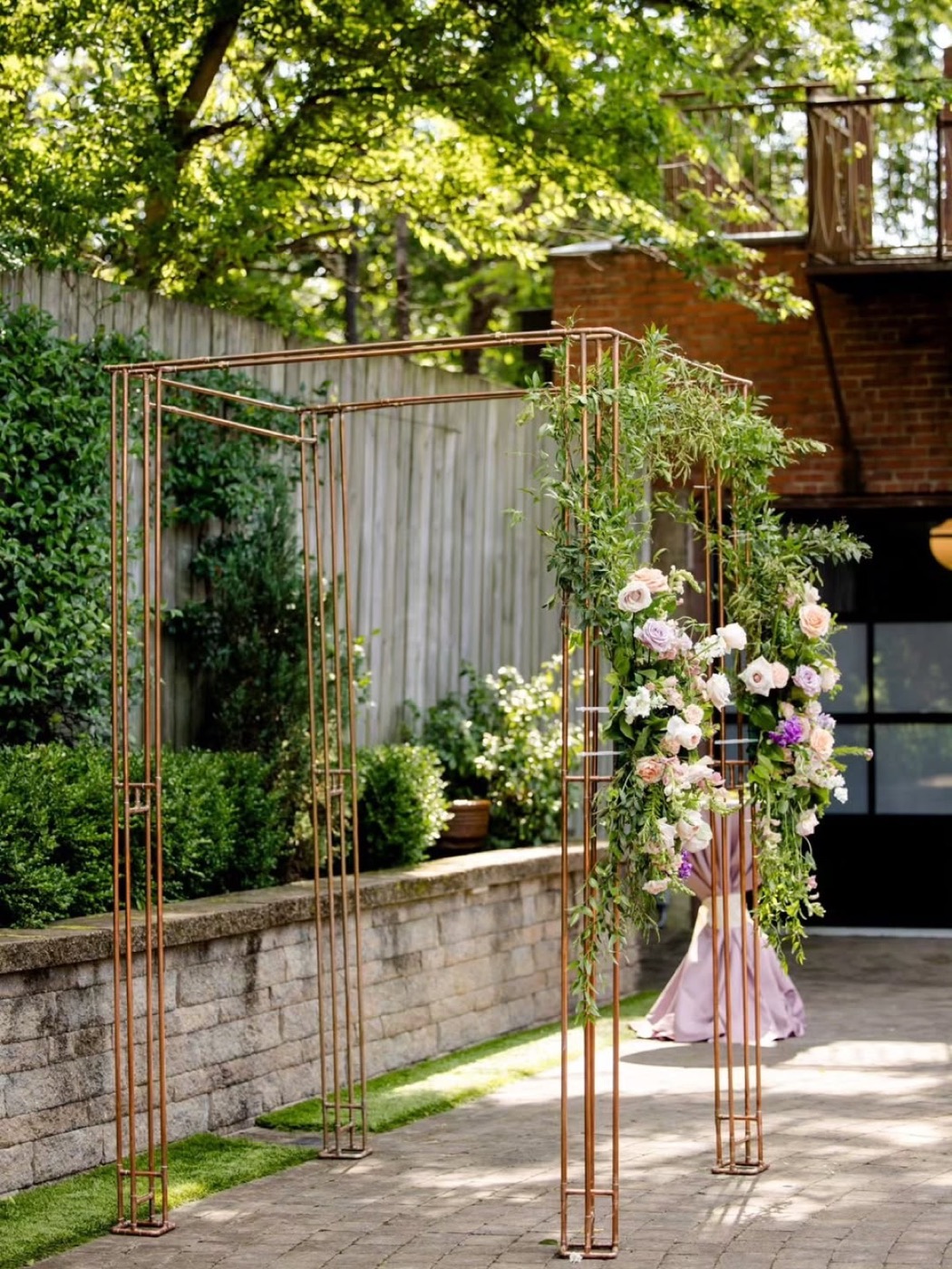 Copper chuppah frame with florals on a brick courtyard