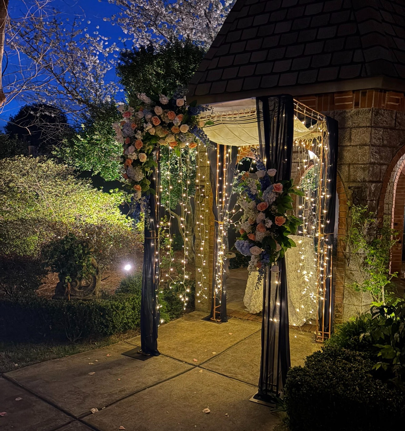Copper chuppah at night with string lights, dark drapery, and florals