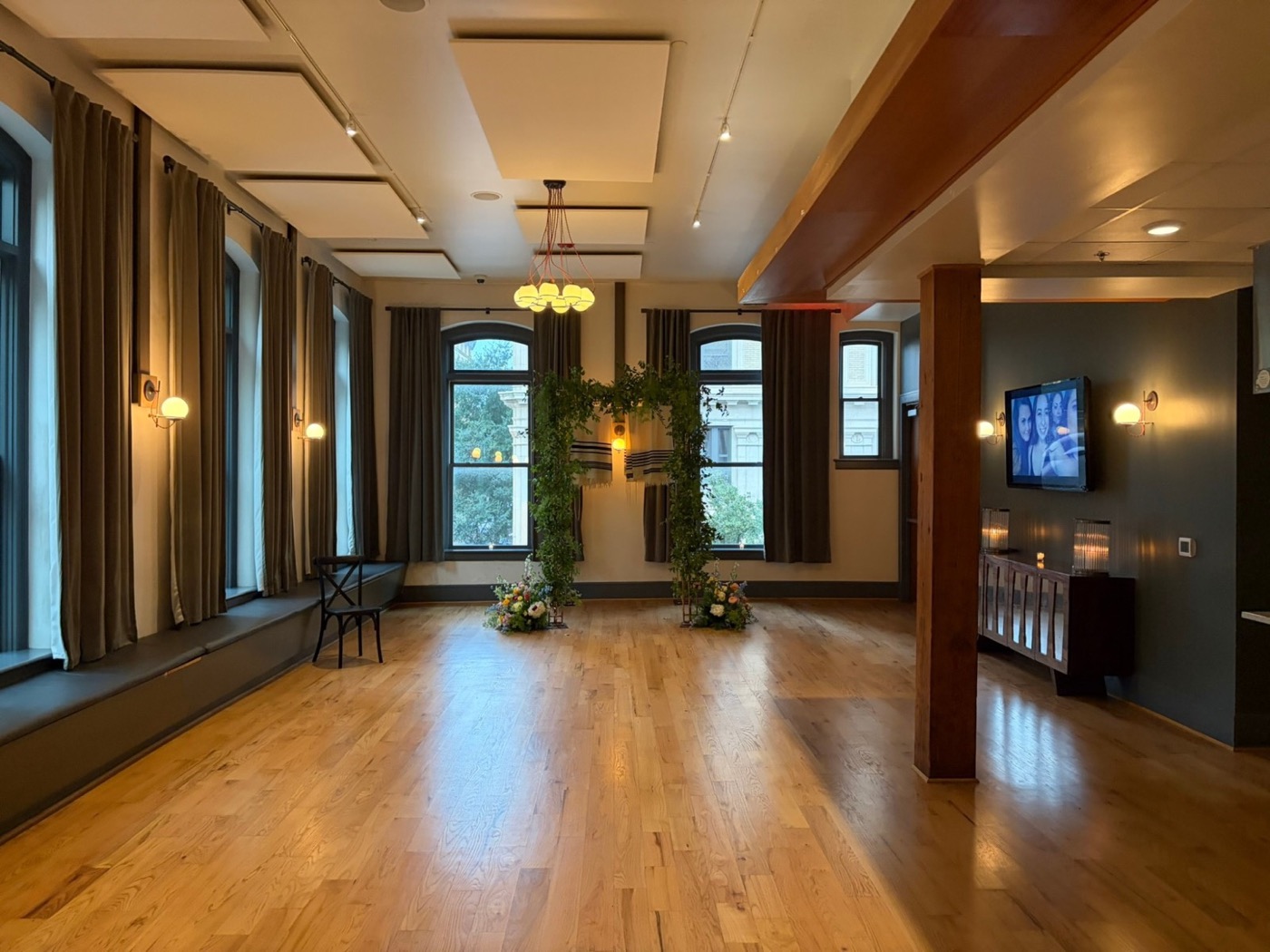 Wide view of a loft event space with the greenery-covered chuppah between two arched windows