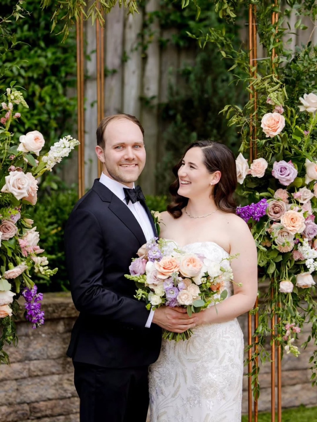 The couple smiling under the copper chuppah at their wedding